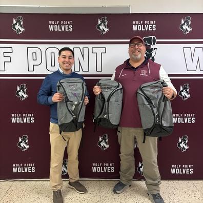Easton Copenhaver (at left) presents new backpacks sponsored by Opportunity Bank of Montana to Wolf Point High School At