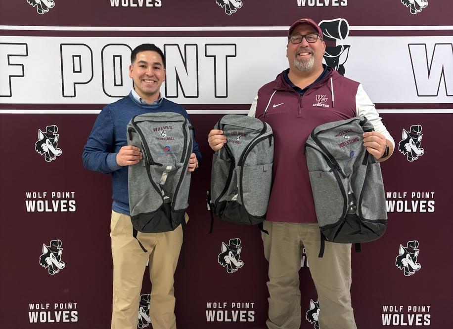 Easton Copenhaver (at left) presents new backpacks sponsored by Opportunity Bank of Montana to Wolf Point High School At