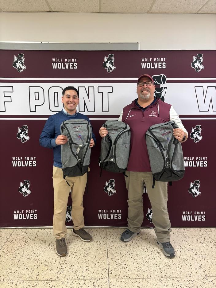 Easton Copenhaver (at left) presents new backpacks sponsored by Opportunity Bank of Montana to Wolf Point High School Athletic Director Eric Peterson to support local student-athletes.